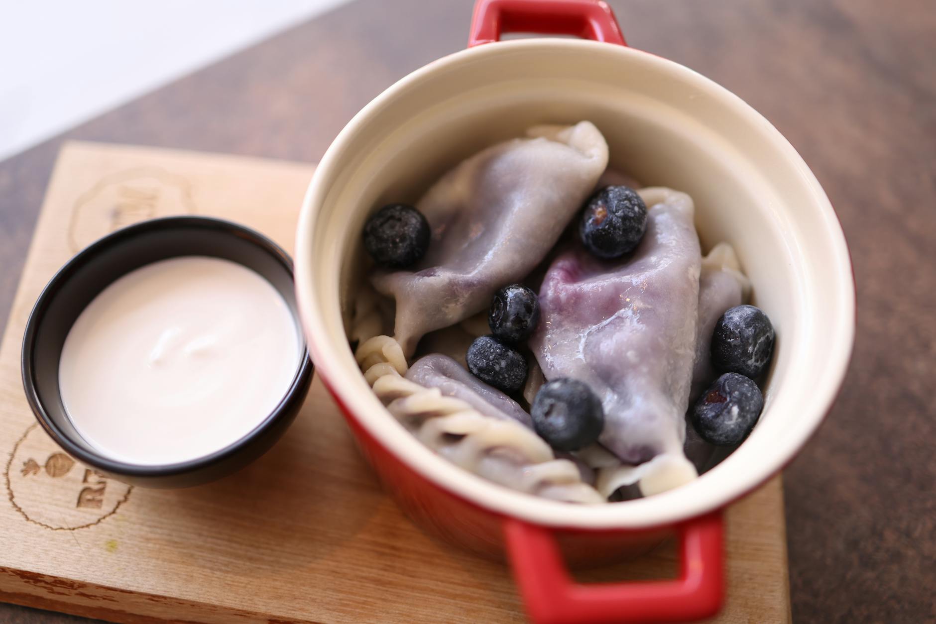 Jagodowe pierogi na talerzu z miseczką śmietany obok